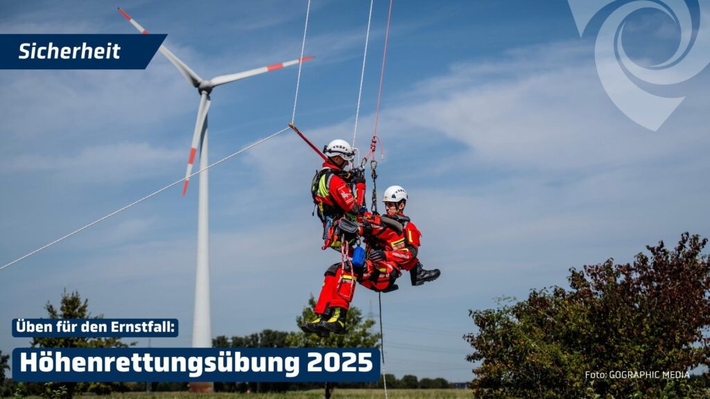 Zwei Angehörige eines Höhenrettungsteams hängen während einer Rettungsübung an Seilen in großer Höhe. Im Hintergrund ist eine Windenergieanlage zu sehen. Eingeblendet sind die Texte „Sicherheit“, „Üben für den Ernstfall“ und „Höhenrettungsübung 2025“. Als Bildquelle ist GOGRAPHIC MEDIA angegeben.
